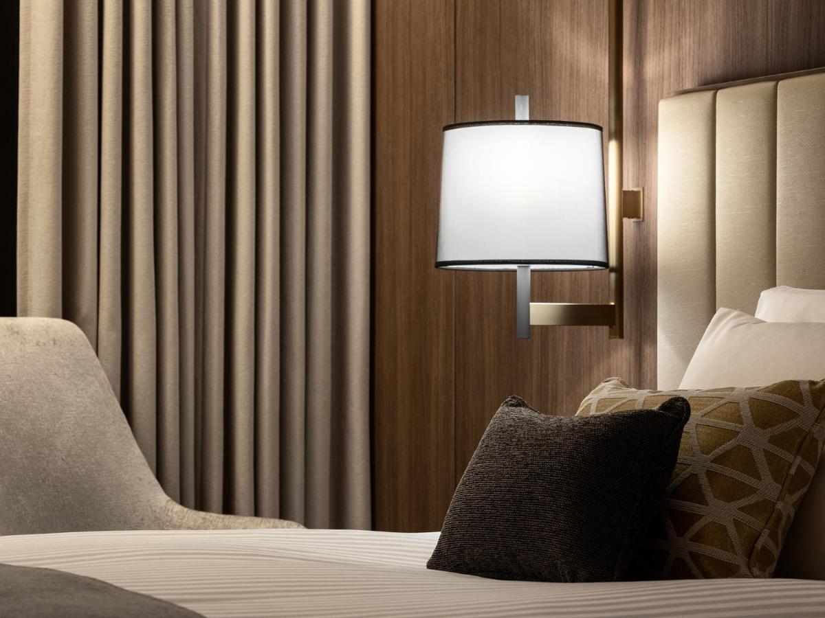 Mitsui Garden Hotel Roppongi Tokyo Premier Екстер'єр фото The photo displays a cozy hotel room setting. It features a neatly made bed with white linens and several decorative pillows. To the side, there’s a stylish bedside lamp mounted on the wall with a round white shade. Behind the lamp, there are elegant