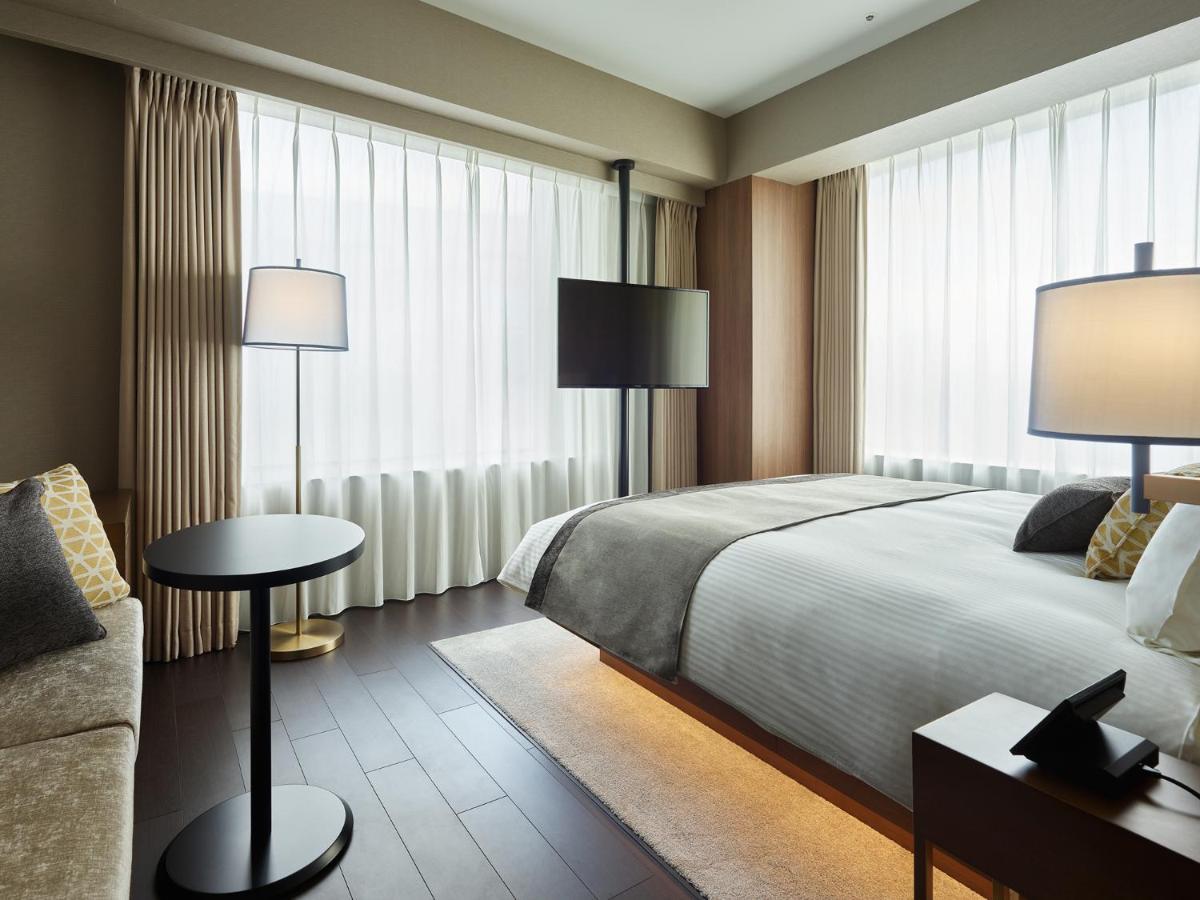 Mitsui Garden Hotel Roppongi Tokyo Premier Екстер'єр фото The photo shows a modern hotel room with a contemporary design. It features a large bed with crisp white linens, sitting against a wall with floor-to-ceiling windows covered by sheer curtains, allowing natural light to filter in. To the side, there's