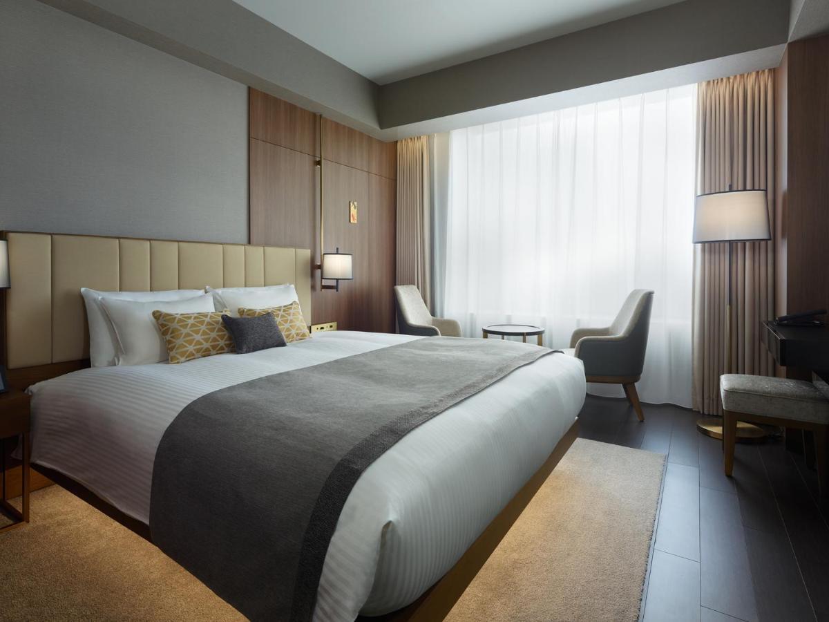 Mitsui Garden Hotel Roppongi Tokyo Premier Екстер'єр фото The photo shows a modern hotel room featuring a large bed with a neatly arranged white and gray bedding. The headboard is upholstered in a light color, adding to the room's contemporary design. On either side of the bed, there are bedside lamps provi