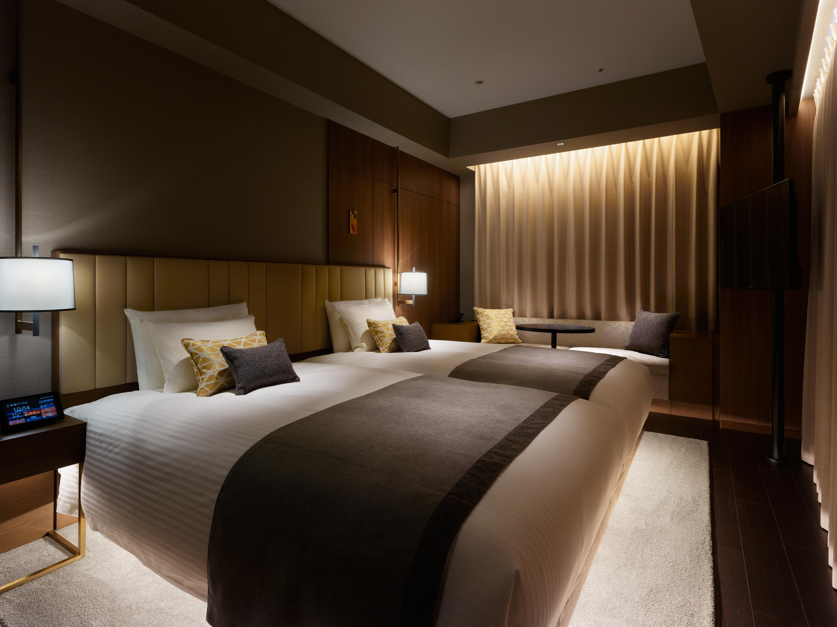 Mitsui Garden Hotel Roppongi Tokyo Premier Екстер'єр фото The photo shows a modern hotel room featuring two beds with plush white linens and decorative pillows. The room has a warm and inviting ambiance, highlighted by soft lighting from lamps and the backlit curtains. There is also a small table with chair