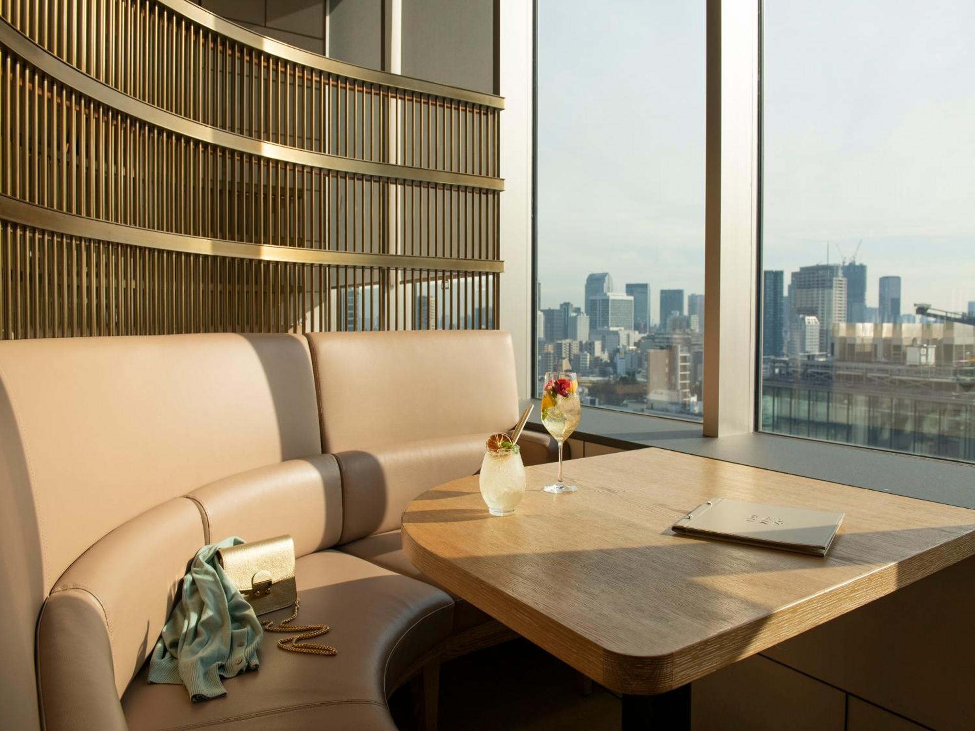 Mitsui Garden Hotel Roppongi Tokyo Premier Екстер'єр фото The photo depicts a cozy, modern seating area with a curved booth that features soft, pale upholstery. A wooden table is positioned in front of the booth, and on the table, there are two elegant drinks garnished with fruit. The setting has large wind