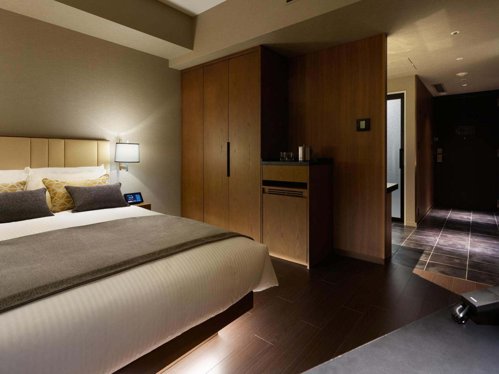 Mitsui Garden Hotel Roppongi Tokyo Premier Екстер'єр фото The photo shows a modern hotel room featuring a neatly made bed with decorative pillows. The room has wooden accents, including a wardrobe and cabinetry, contributing to a warm ambiance. A bedside lamp is on one side of the bed, and there's a small a